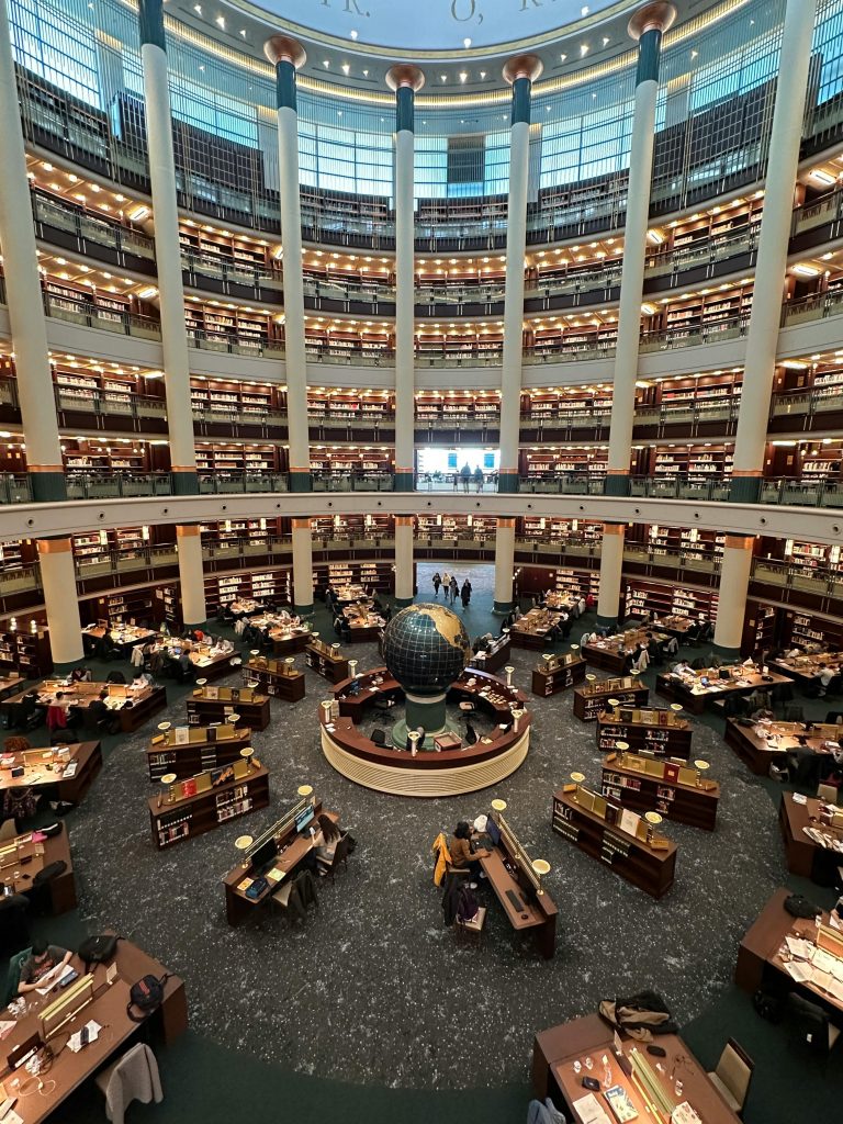 A large modern library interior with a central globe and multiple reading desks. Aerial view.